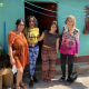 4 colorfully dressed women posing in front of a turquoise house